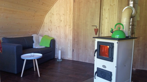 Interno della sistemazione glamping Vollmershof - Lodge Zwarte Woud con divano e stufa a legna.