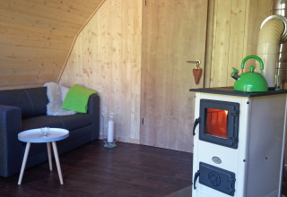 Gemütlicher Innenraum der Glamping-Unterkunft Vollmershof - Lodge Zwarte Woud mit Ofen und Sofa.