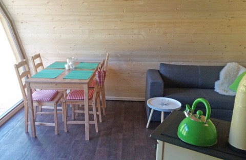 Innenansicht der Glamping-Unterkunft ‘Vollmershof - Lodge Zwarte Woud’ mit Esstisch, Sofa und Teekanne.