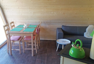 Interior del alojamiento glamping ‘Vollmershof - Lodge Zwarte Woud’ con mesa de comedor, sofá y tetera.