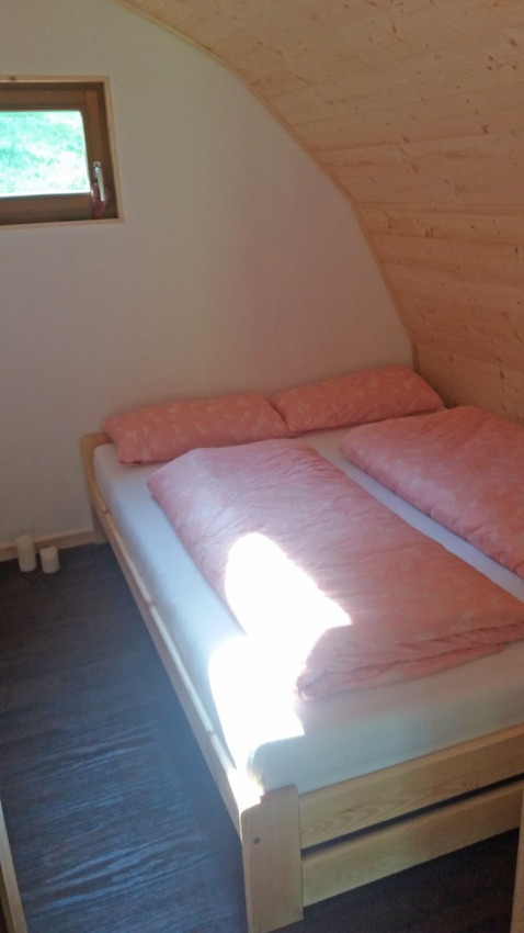 Sfeervolle houten slaapkamer met tweepersoonsbed en roze dekbed in Vollmershof - Lodge Zwarte Woud.