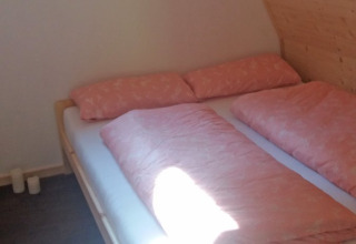 Knusse houten kamer met tweepersoonsbed en roze beddengoed in Vollmershof - Lodge Zwarte Woud.