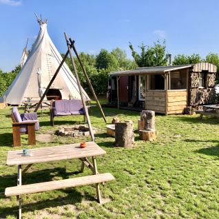 Zona de glamping con tipi, cabaña de madera y asientos al aire libre en Glamping 't Buitenland.