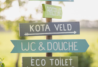 Buntes Schild mit Wegweisern zu Yurtfeld, Parkplatz, Kota Feld, WC & Dusche und Öko-Toilette beim Glamping.