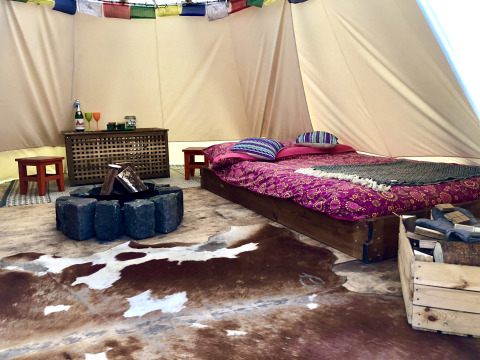 Interior de tienda glamping con cama doble, alfombra, zona de fuego y decoración rústica y colorida.