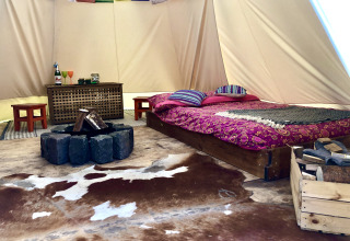 Interior de tienda glamping con cama doble, alfombra, zona de fuego y decoración rústica y colorida.