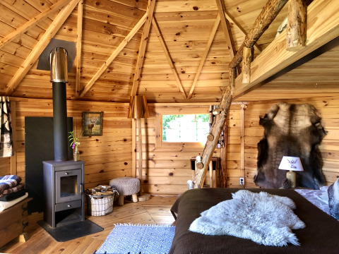 Innenansicht einer gemütlichen Holzhütte mit Kamin, Fellen und rustikaler Einrichtung für Glamping.