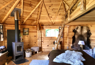 Vista interior de una acogedora cabaña de madera con chimenea, pieles y decoración rústica para glamping.