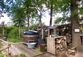 Outdoor hot tub and rustic wooden decor at Glamping 't Buitenland surrounded by trees and log piles.