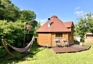 Glamping accommodation: Finnish kota cabin with deck chairs and hammock set in a sunny, lush garden.