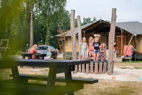 Kinderen spelen bij een safaritent op Camping de Pallegarste in Overijssel, volwassenen ontspannen aan picknicktafels.