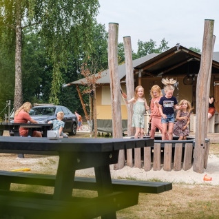 Kinderen spelen voor een safaritent aan Camping de Pallegarste in Overijssel, volwassenen zitten aan de tafels.