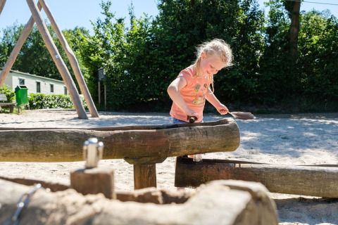 Een kind speelt op een houten speelplaats bij Camping de Pallegarste - Safaritenten Overijssel op een zonnige dag.