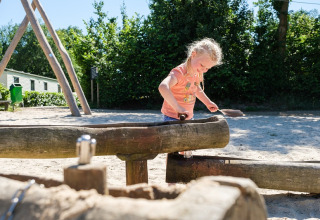 Een kind speelt op een houten speelplaats bij Camping de Pallegarste - Safaritenten Overijssel op een zonnige dag.
