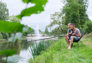 Far og søn fisker ved en sø ved Camping de Pallegarste, Safaritenten Overijssel, omgivet af natur.