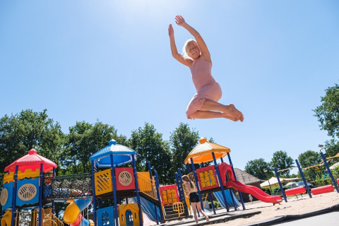 Mujer con vestido rosa salta alto en el parque de Camping de Pallegarste, Safaritenten Overijssel, día soleado
