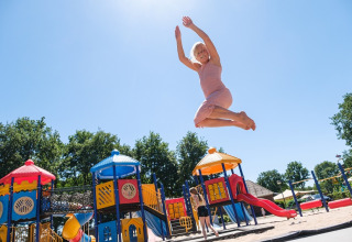 Mujer con vestido rosa salta alto en el parque de Camping de Pallegarste, Safaritenten Overijssel, día soleado