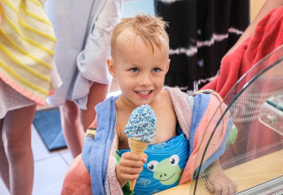 Ein fröhliches Kind mit nassen Haaren genießt ein Eis in einem Safarizelt auf Camping de Pallegarste.