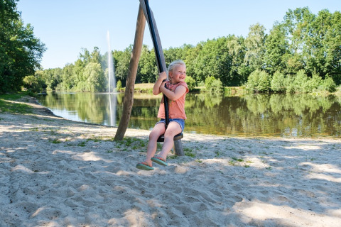 Een kind speelt op een schommel bij het meer op Camping de Pallegarste - Safaritenten Overijssel, Nederland.