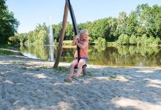Een kind speelt op een schommel bij het meer op Camping de Pallegarste - Safaritenten Overijssel, Nederland.
