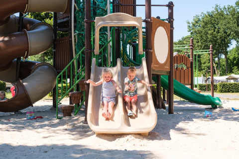 Deux enfants s'amusent sur un toboggan de l'aire de jeux au Camping de Pallegarste Safaritenten Overijssel, journée ensoleillée.
