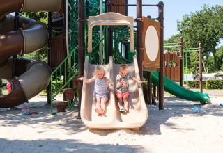 Zwei Kinder rutschen auf einem Spielplatz bei Camping de Pallegarste Safaritenten Overijssel an einem sonnigen Tag.