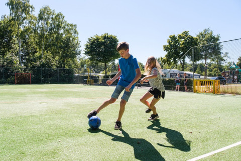 Dos niños juegan al fútbol en el área de juegos de Camping de Pallegarste - Safaritenten Overijssel bajo el sol.