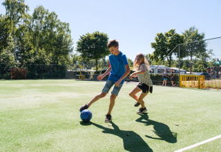 Two children play soccer on the playground at Camping de Pallegarste - Safaritenten Overijssel under the sun.