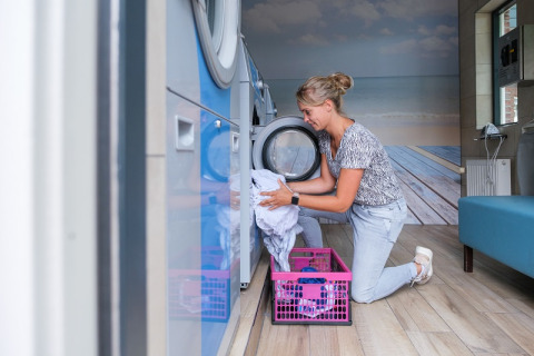 Kvinde lægger vasketøj i maskine på Camping de Pallegarste - Safaritenten Overijssel, moderne vaskeri.