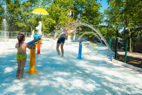Kinder spielen im Wasserpark des Chianti Glamping Resort, umgeben von Bäumen bei sonnigem Wetter.