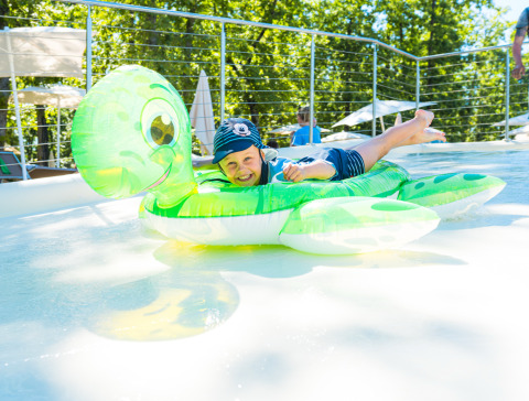 Een kind speelt op een schildpad opblaasfiguur in het zwembad bij Chianti Glamping Resort - Safaritenten Toscane.