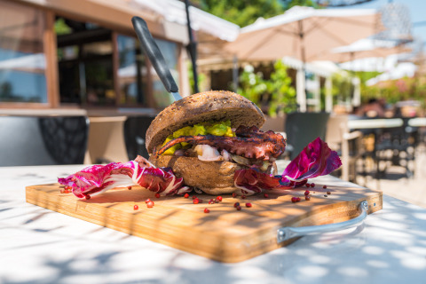 Sandwich gourmet au poulpe et salade sur planche à découper, en terrasse d’un restaurant de glamping en Toscane.