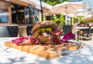 Panino gourmet con polpo e insalata su tagliere di legno, servito all’aperto in un ristorante di glamping in Toscana.