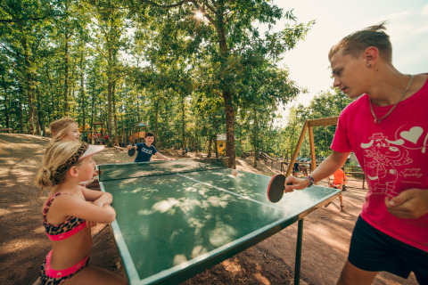 Des enfants jouent au ping-pong en plein air au Chianti Glamping Resort, entourés d’arbres et de nature.