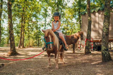 Enfant sur un poney au Chianti Glamping Resort en Toscane, entouré d’arbres et de tentes safari.