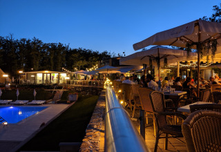 Outdoor dining area at Chianti Glamping Resort in Tuscany at dusk, near a pool and illuminated by string lights.