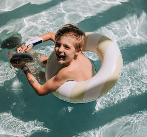 Garçon souriant joue dans la piscine avec une bouée à Recreatiepark de Achterste Hoef - Safaritenten Brabant.