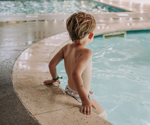 Child sits at the edge of an indoor pool at Recreatiepark de Achterste Hoef Safaritenten Brabant.