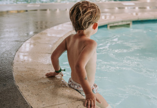 Bambino seduto sul bordo di una piscina coperta al Recreatiepark de Achterste Hoef Safaritenten Brabant.
