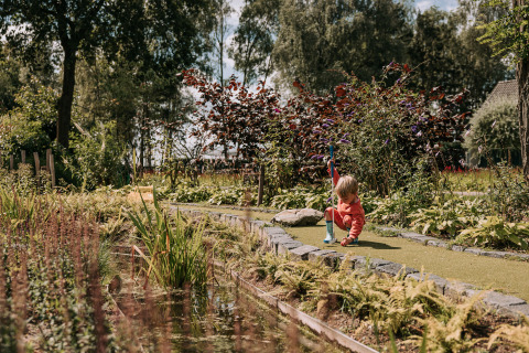 Enfant jouant au mini-golf à Safaritenten Brabant, entouré de verdure au Recreatiepark de Achterste Hoef.