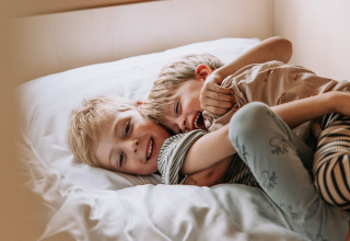 Twee kinderen spelen en lachen samen op een bed in een tent bij Recreatiepark de Achterste Hoef - Safaritenten Brabant.
