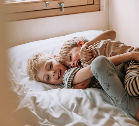 Twee kinderen lachen en spelen op een bed in een safaritent bij Recreatiepark de Achterste Hoef - Safaritenten Brabant.