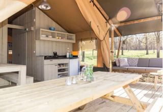 Binnenzicht op Trixi Ferienpark safaritent met houten tafel, keuken en gezellige loungezetel.