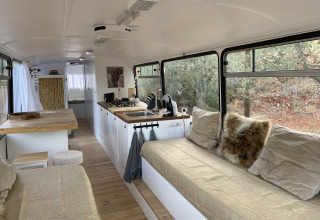Innenraum des Algarve Olive Tree Lodge Glamping-Schulbusses mit Küche, Sofa und Blick ins Grüne.