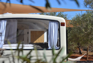 Innenansicht eines umgebauten Schulbusses mit weißen Vorhängen, Glamping in der Algarve Olive Tree Lodge.