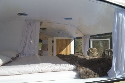Binnenkant van een glamping-schoolbus met bed, gordijnen en ramen in de Algarve Olive Tree Lodge.