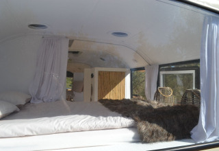 Indvendigt billede af en hyggelig glampingbus med seng, gardiner og naturligt sollys, Algarve.