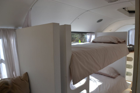 Indvendig udsigt af et glamping skolebus-værelse med køjesenge og bløde hvide gardiner i Algarve.