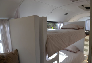 Interior view of a glamping school bus room with bunk beds and soft white curtains in the Algarve.