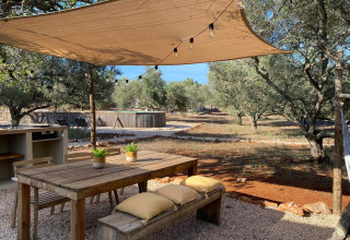 Gemütlicher Essbereich im Freien bei Algarve Olive Tree Lodge mit Sonnensegel, Holztisch und Olivenbäumen.